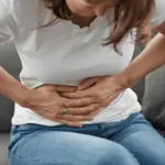 Frau hält sich gekrümmt den Bauch: Darstellung starker, krampfartiger Magenschmerzen und Unwohlsein.