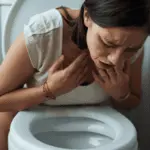 Frau mit starker Übelkeit und Brechreiz über einer Toilette (Symptom der Gastroparese/Reizmagen).